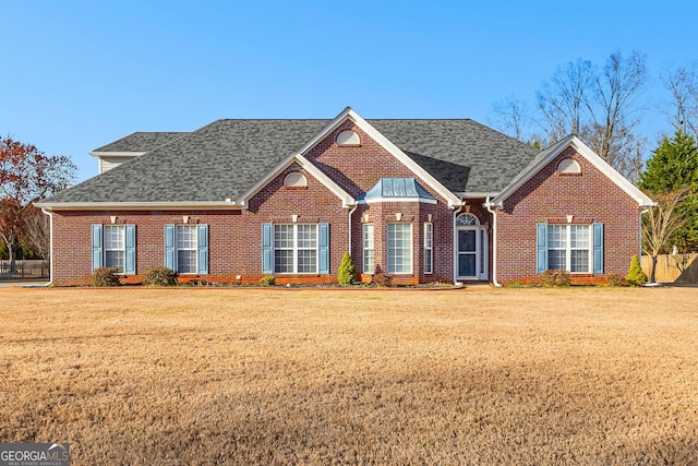 view of front of property featuring brick siding, roof with shingles, and a front yard