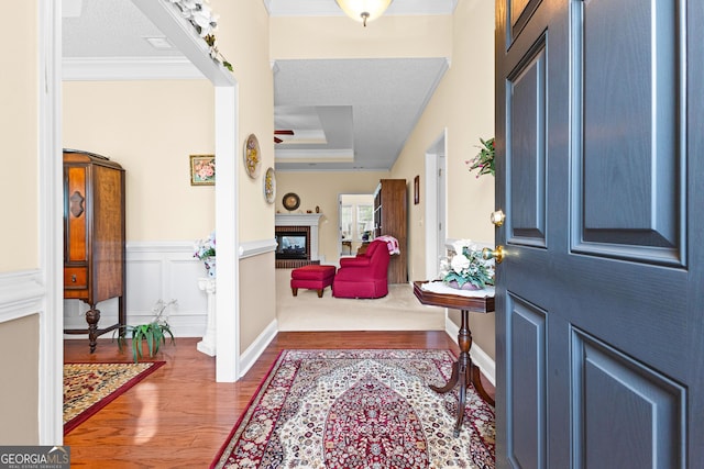 foyer featuring a tray ceiling, wood finished floors, a glass covered fireplace, crown molding, and a decorative wall