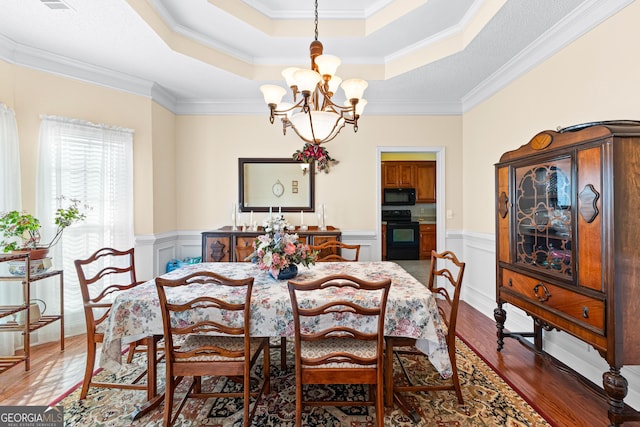 dining room featuring a wainscoted wall, a notable chandelier, wood finished floors, crown molding, and a raised ceiling