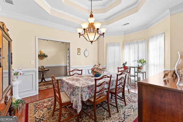 dining area with visible vents, a tray ceiling, wood finished floors, crown molding, and a chandelier