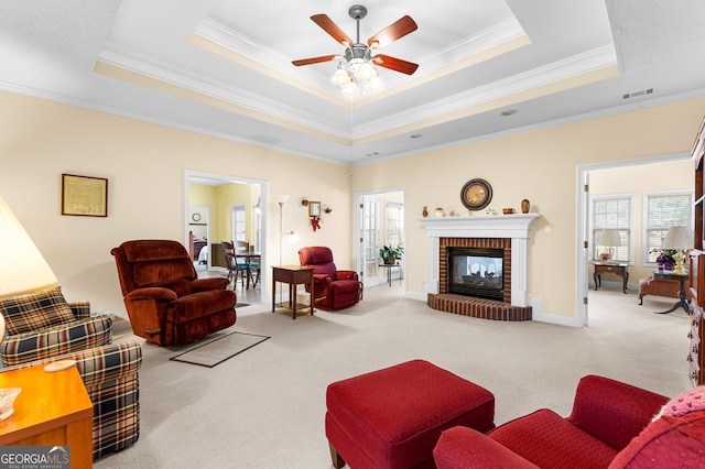 carpeted living room with visible vents, a raised ceiling, a brick fireplace, and ornamental molding