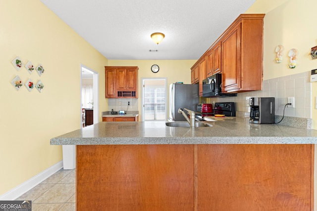 kitchen featuring a sink, backsplash, freestanding refrigerator, black microwave, and stove