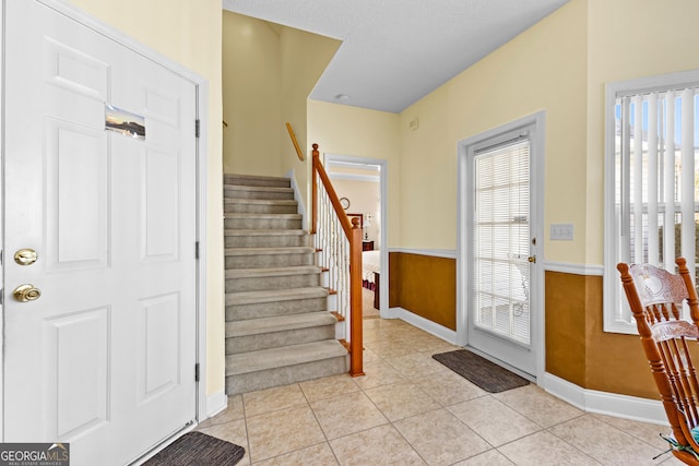 entrance foyer with light tile patterned floors, a wainscoted wall, a healthy amount of sunlight, and stairs