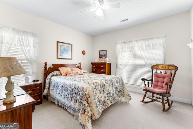 bedroom featuring a textured ceiling, light colored carpet, visible vents, and ceiling fan