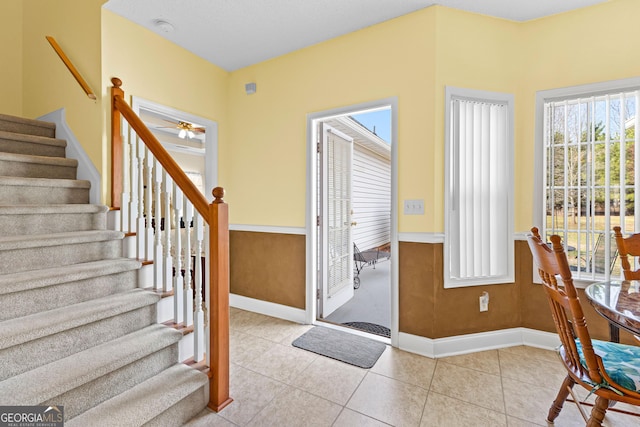 tiled foyer entrance featuring stairs, baseboards, and a wainscoted wall