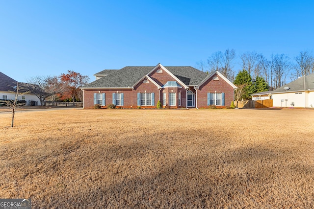 view of front of home with brick siding, roof with shingles, a front lawn, and fence