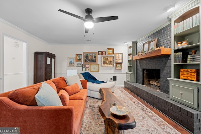 living room with built in shelves, wood finished floors, visible vents, a fireplace, and crown molding