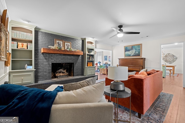 living room featuring visible vents, ornamental molding, wood finished floors, a brick fireplace, and ceiling fan