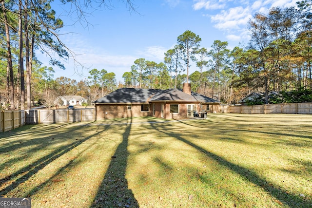 rear view of house featuring brick siding, a fenced backyard, a chimney, and a yard