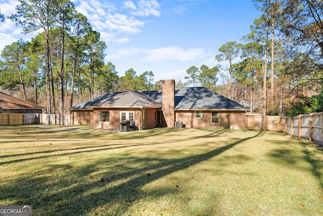 back of property with a lawn, central AC, a fenced backyard, brick siding, and a chimney