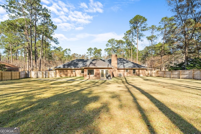 back of property with a yard, a fenced backyard, a chimney, dirt driveway, and brick siding