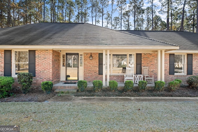 ranch-style house featuring brick siding, a porch, a front yard, and roof with shingles