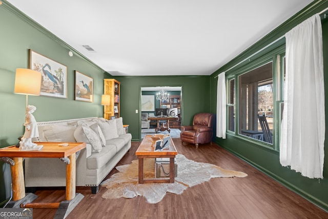 living room featuring an inviting chandelier, crown molding, wood finished floors, and visible vents