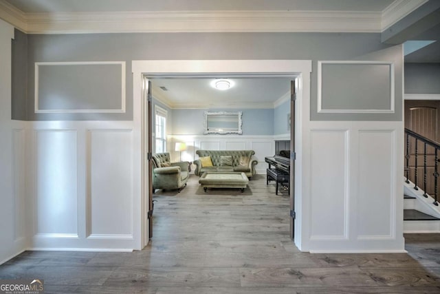 hall with stairs, a decorative wall, wood finished floors, and ornamental molding