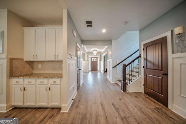 corridor with stairs, light wood-style flooring, and visible vents