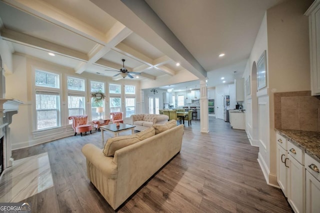 living area featuring a ceiling fan, wood finished floors, coffered ceiling, beam ceiling, and a fireplace with flush hearth