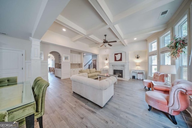 living area featuring visible vents, light wood finished floors, arched walkways, beamed ceiling, and a decorative wall