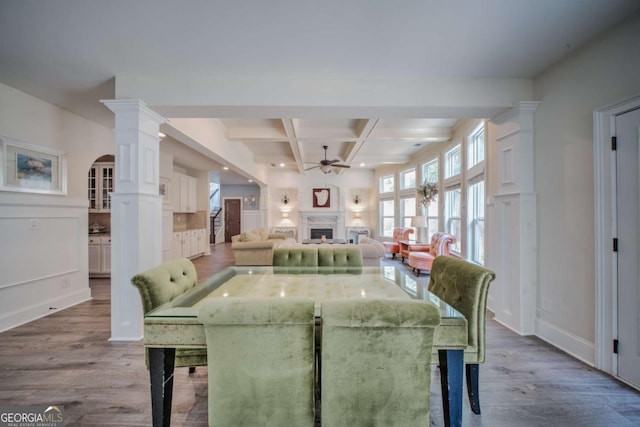 unfurnished dining area featuring beamed ceiling, coffered ceiling, wood finished floors, a fireplace, and decorative columns