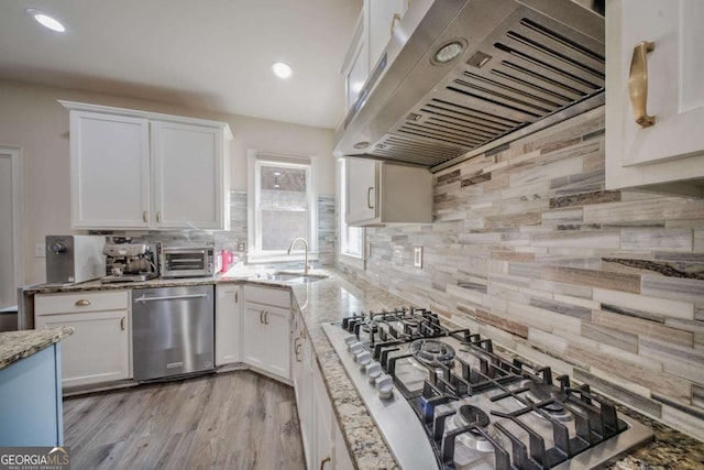 kitchen featuring range hood, appliances with stainless steel finishes, white cabinets, and a sink