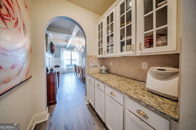 kitchen featuring backsplash, coffered ceiling, dark wood-style floors, arched walkways, and glass insert cabinets