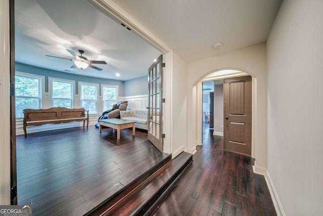 hallway featuring baseboards, arched walkways, and dark wood-type flooring