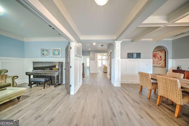 foyer entrance featuring crown molding, light wood-type flooring, wainscoting, a decorative wall, and ornate columns