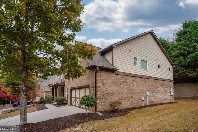 view of side of home with brick siding, an attached garage, roof with shingles, a yard, and driveway