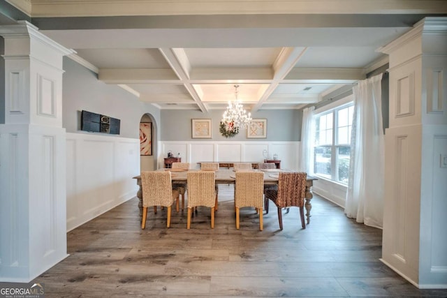 dining space with wood finished floors, coffered ceiling, beam ceiling, arched walkways, and a notable chandelier