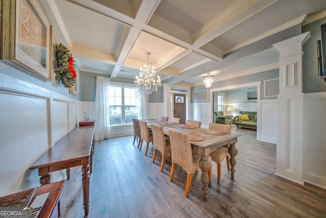 dining area featuring beamed ceiling, coffered ceiling, wood finished floors, a decorative wall, and a chandelier