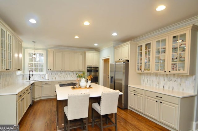 kitchen with dark wood-style flooring, a sink, stainless steel appliances, a kitchen breakfast bar, and a center island