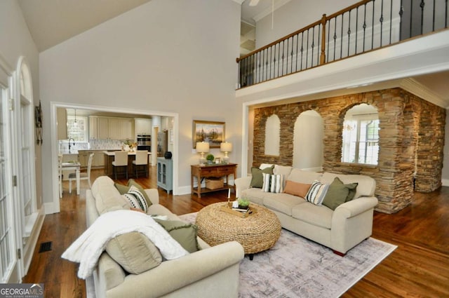 living area with baseboards, wood finished floors, visible vents, and high vaulted ceiling