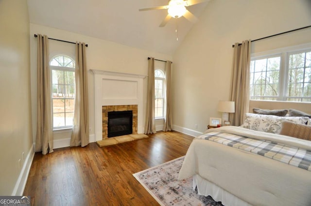 bedroom featuring baseboards, lofted ceiling, a stone fireplace, wood finished floors, and a ceiling fan