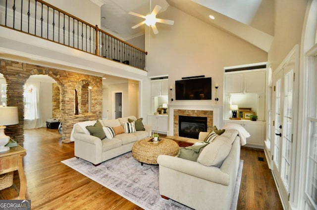 living room with high vaulted ceiling, wood finished floors, a fireplace, ceiling fan, and ornate columns