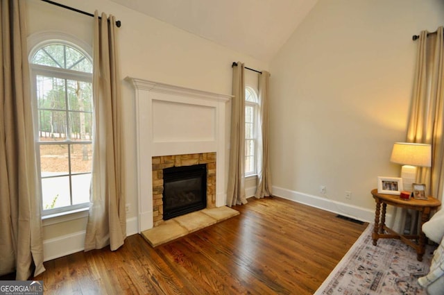 living area featuring visible vents, dark wood-type flooring, baseboards, lofted ceiling, and a stone fireplace