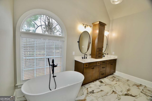 full bath featuring lofted ceiling, double vanity, a freestanding tub, marble finish floor, and a sink