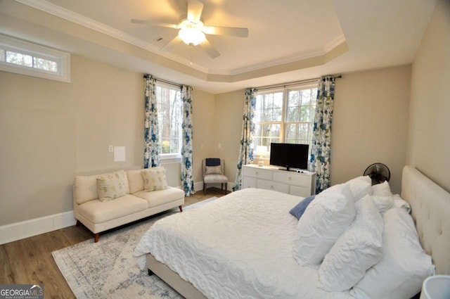 bedroom with a ceiling fan, wood finished floors, baseboards, a tray ceiling, and crown molding