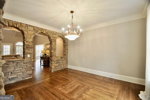 unfurnished dining area featuring arched walkways, crown molding, baseboards, and wood finished floors