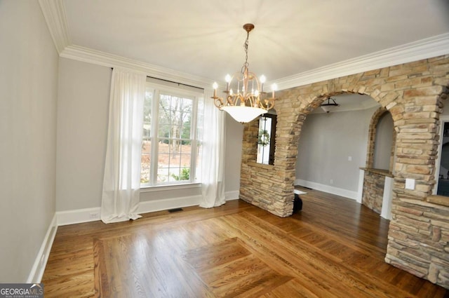 unfurnished dining area with wood finished floors, baseboards, visible vents, crown molding, and a chandelier