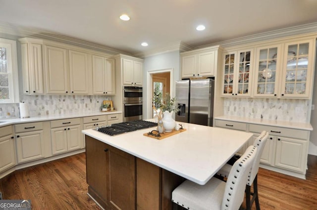 kitchen with dark wood-style floors, a kitchen island, stainless steel appliances, and glass insert cabinets