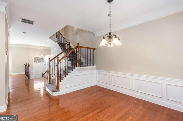 stairs with an inviting chandelier, crown molding, wood finished floors, and visible vents