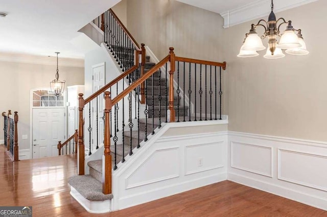 staircase featuring crown molding, an inviting chandelier, and wood finished floors