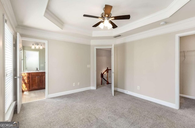 unfurnished bedroom featuring a spacious closet, visible vents, light colored carpet, ornamental molding, and a raised ceiling