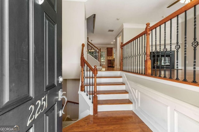 entrance foyer with visible vents, crown molding, stairs, wood finished floors, and a decorative wall