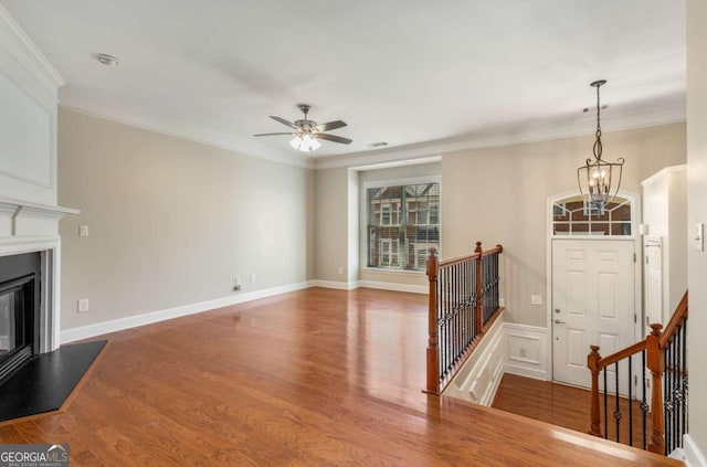 unfurnished living room with a glass covered fireplace, crown molding, ceiling fan with notable chandelier, and wood finished floors