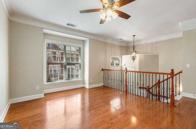 unfurnished room featuring crown molding, wood finished floors, visible vents, and baseboards