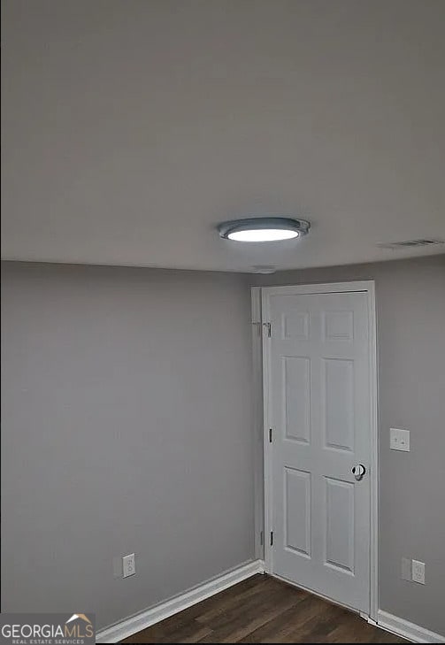 empty room with visible vents, dark wood-type flooring, and baseboards