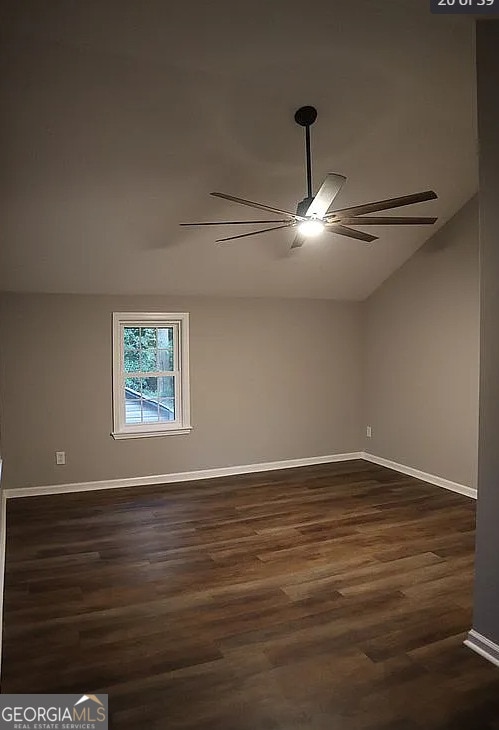 empty room with a ceiling fan, vaulted ceiling, dark wood-style floors, and baseboards