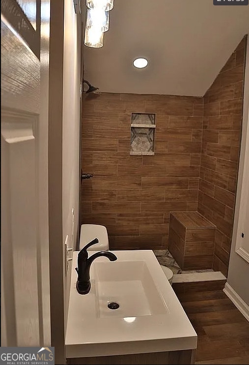 bathroom featuring a tile shower, wood finished floors, and a sink