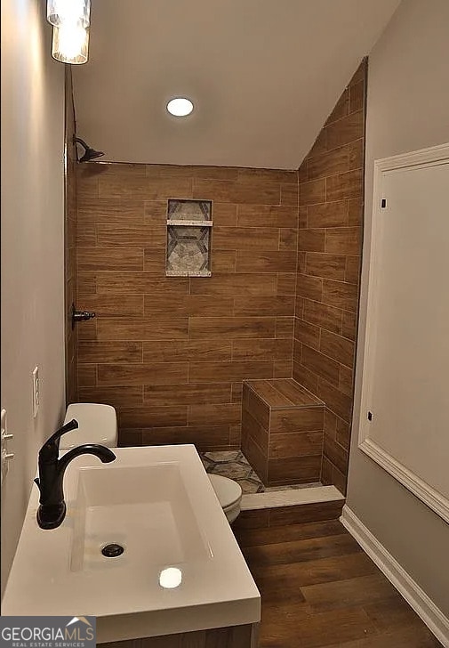 bathroom with a sink, toilet, wood finished floors, and a tile shower