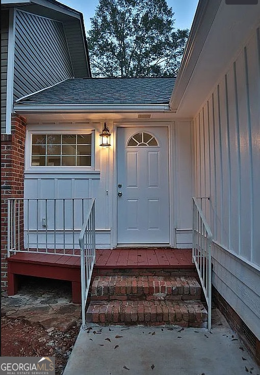 doorway to property with brick siding and a shingled roof